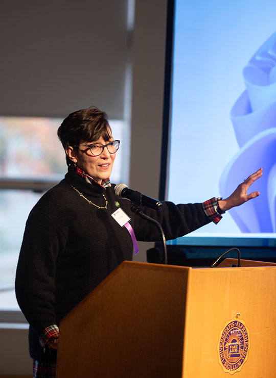 woman with short hair and glasses talking at a podium