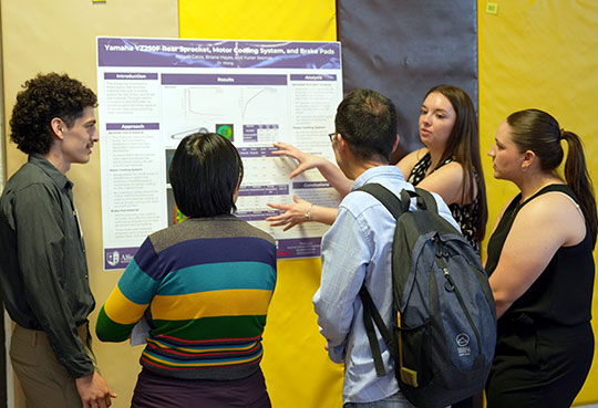 group of five people, discussing a poster