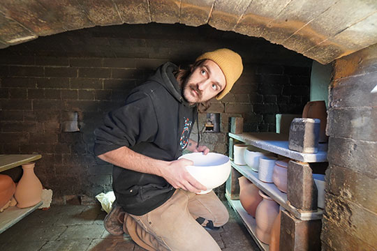 man with hat inside pottery kiln with some pots