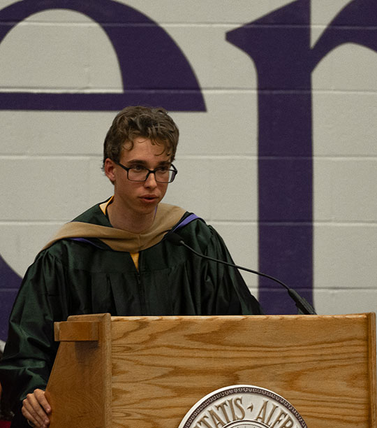young mad with glasses, wearing robe, talking at podium