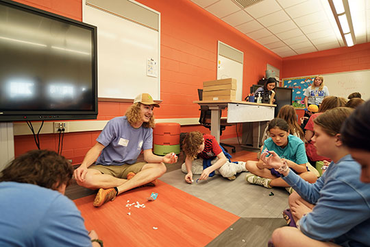 young man with long hair and hat talking to children
