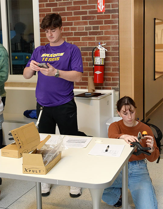 two students, one sitting at a desk operating a small catapult