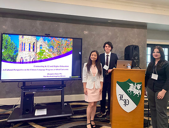 two women and a man standing by a lectern and projector screen