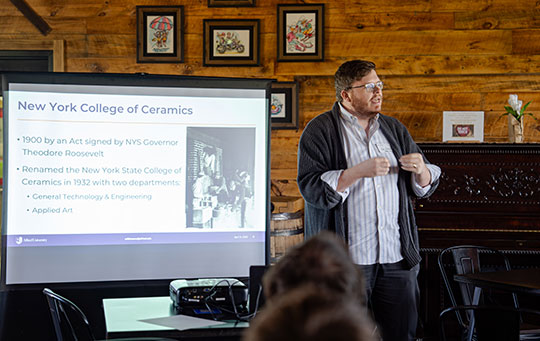 man with glasses talking in front of a screen
