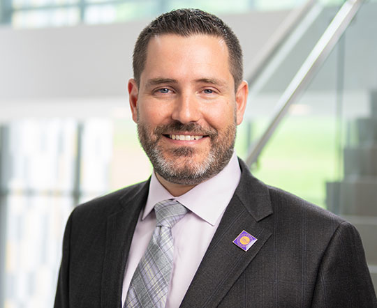headshot of man with beard, wearing suit and tie, smiling