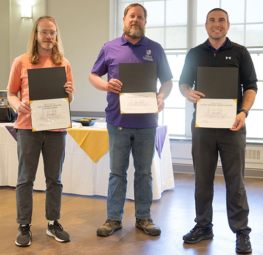 three men standing, holding certificates