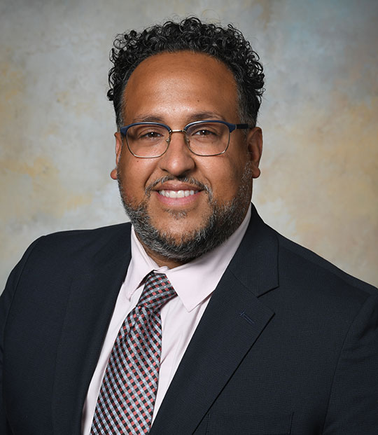 headshot of man with glasses, in suit and tie