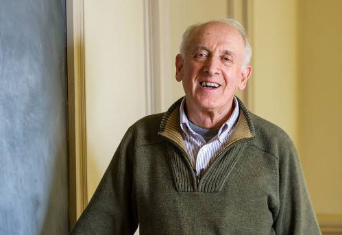 headshot of man with white hair in sweater smiling