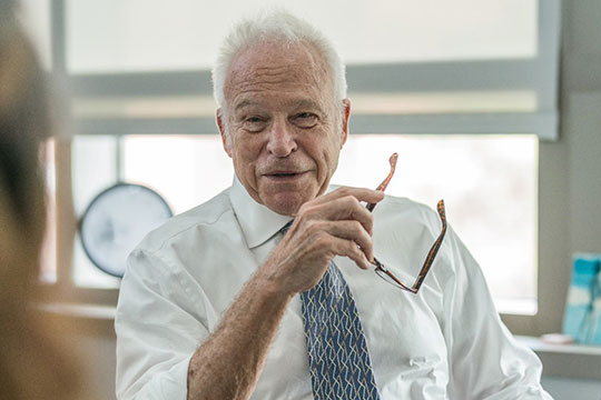 headshot of man in shirt and tie, holding eyeglasses