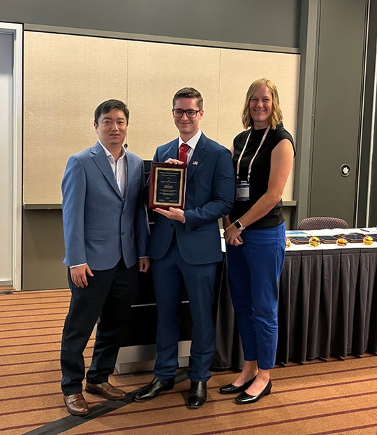 photo of two men and a woman, one man holding a plaque
