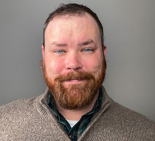 headshot of man with beard wearing sweater and smiling