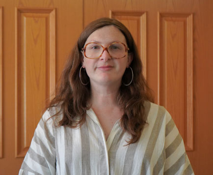 headshot of woman with white blouse, long brown hair, and glasses