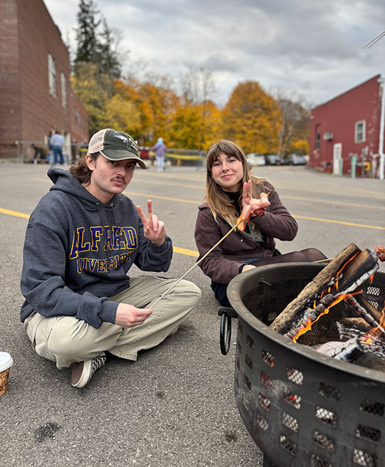 two people sitting by a fire eating a snack