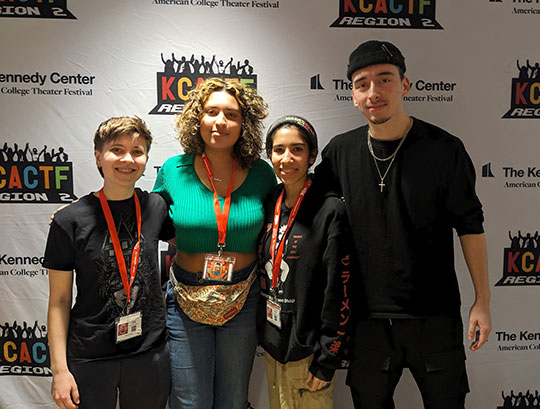 four people, students, standing in front of banner