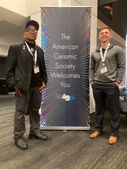 Two men standing in front of a sign
