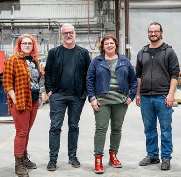four people standing next to each other in a foundry