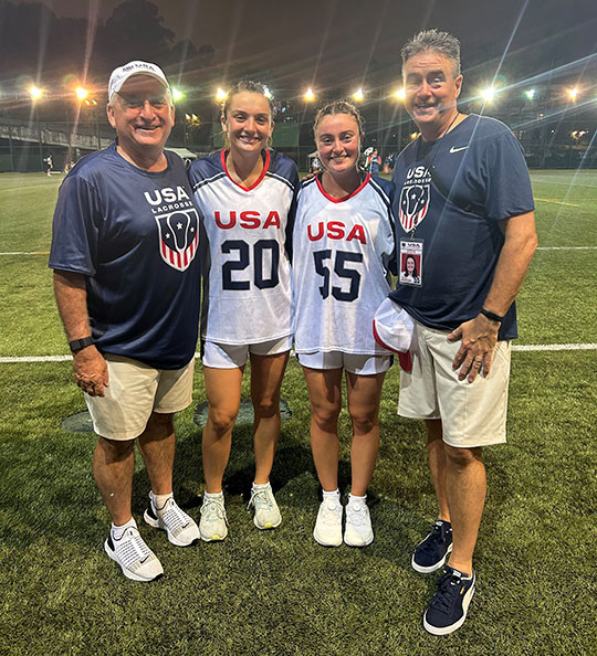 four people, two men and two women, smiling. women are dressed in lacrosse uniforms