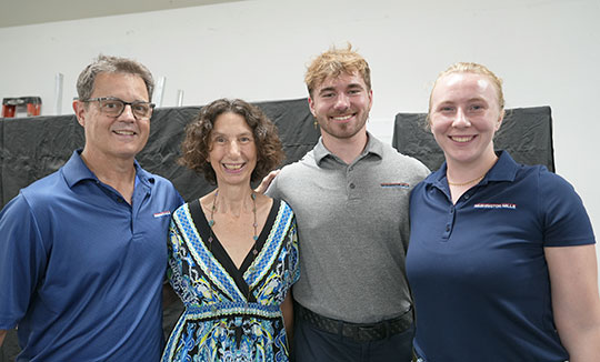 four people, two men and two women, standing side by side, smiling