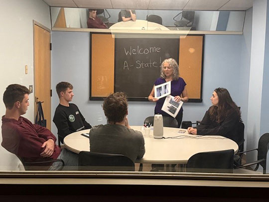 woman standing and talking to a group of people sitting around a table