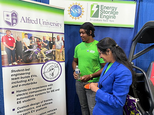 Two people stand near an Alfred University engineering project display, with banners promoting energy storage. They appear engaged and focused.
