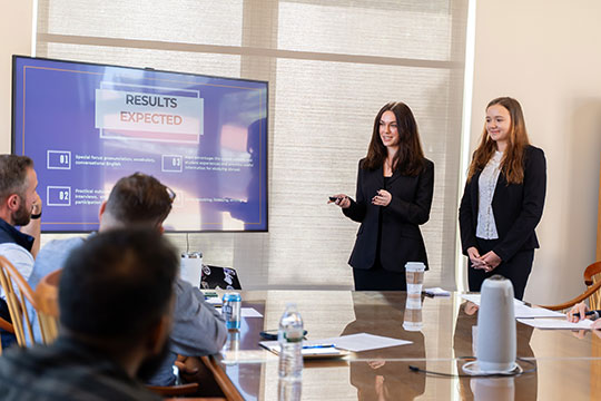 two young women standing and talking to a group
