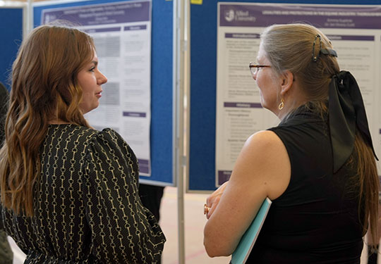 a young woman talking to another woman in front of a poster