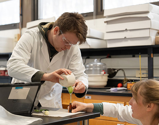 Alfred University biology professor Cat Clarke (right) assists Wellsville High School student Evan Billings as he filters a spinach acetone mixture to extract chlorophyll during a photosynthesis lab workshop.