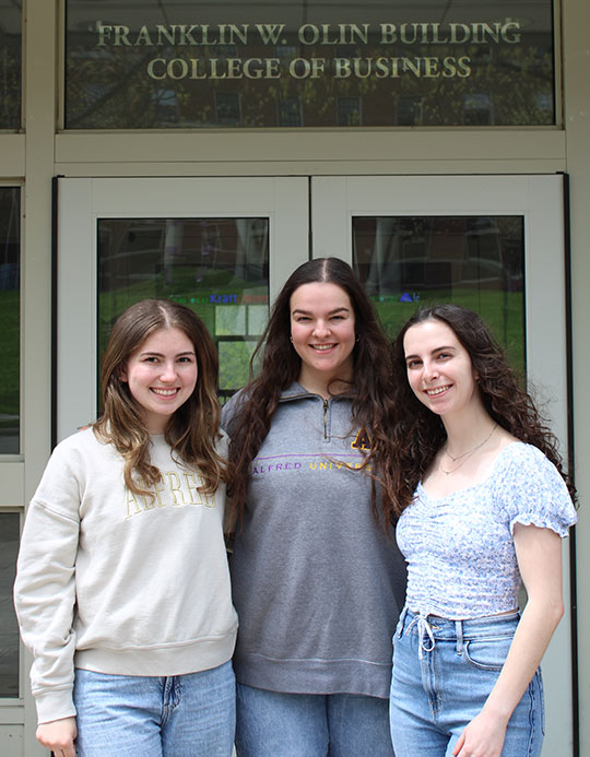 three young women standing in front of a building, smiling