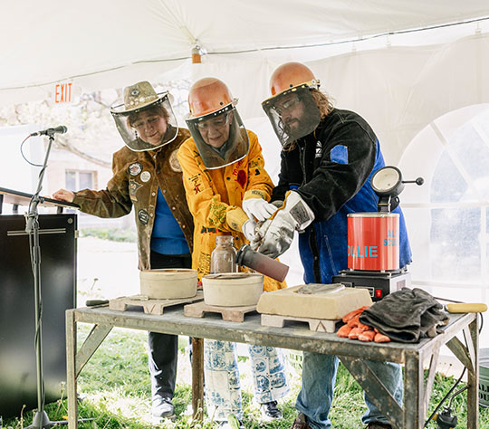 three people pouring hot metal into a form
