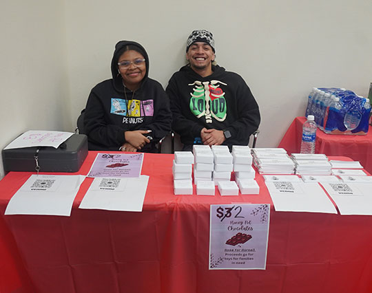 Two Alfred University Marketing Club students smiling while selling Honey Pot Chocolates at a fundraising table.