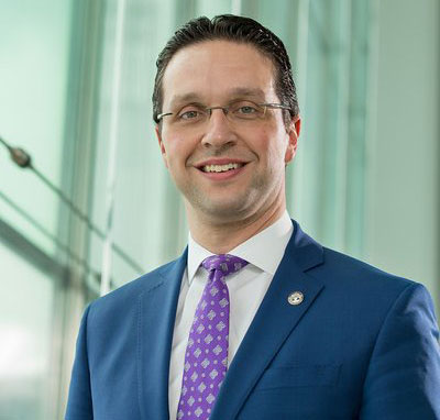 headshot of man in suit and tie with glasses, smiling
