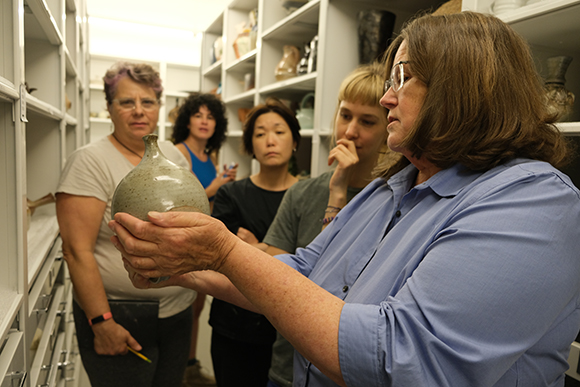 Susan Kowalczyk, Curator of Collections and Director of Research at the Alfred Ceramic Art Museum, showing a ceramic vessel to students during a lesson in the museum’s collection storage.