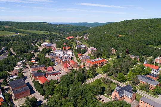 Aerial view of Alfred University campus surrounded by hills and greenery on a sunny day.