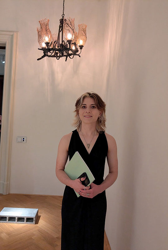 woman with short hair in black dress standing in front of a chandelier