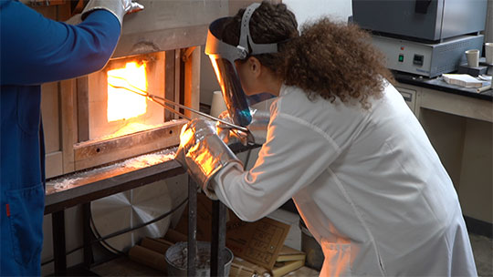Student wearing protective gear working with molten material in a high-temperature furnace during an engineering lab at Alfred University.
