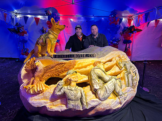 two men standing behind giant jack-o-lantern