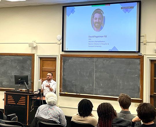 man standing in front of a projector, talking to some people