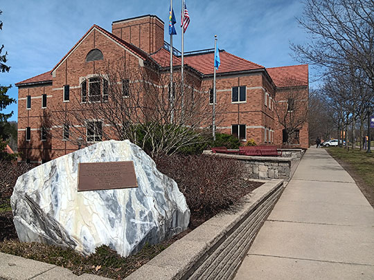 park with marble slab, benches, flagpoles with building behind it