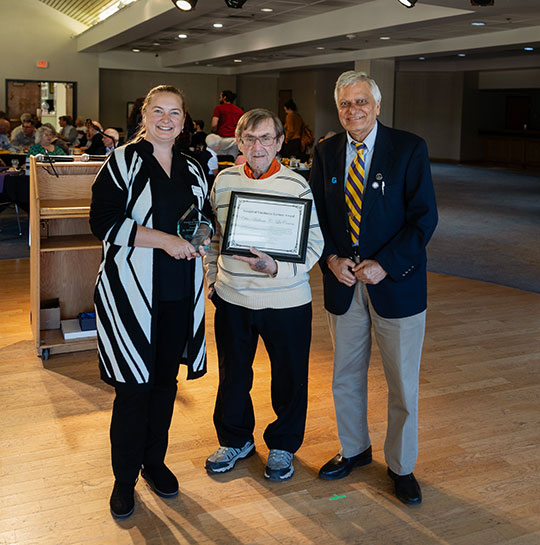 three people, woman and two men, one holding a certificate, standing in a row, smiling