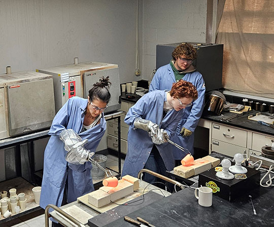 three people in a lab working with molten glass