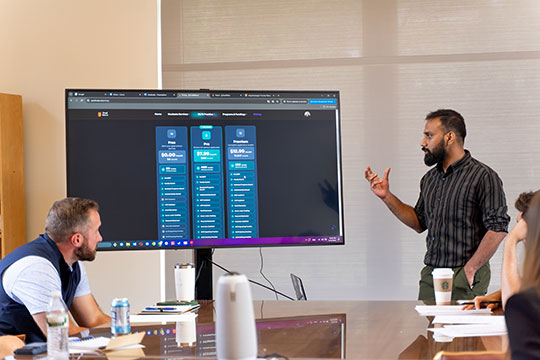 A student presents a project on a large screen to classmates and faculty during a business or technology class discussion.