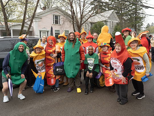Alfred University staff and community members dressed as hot dogs, pickles, ketchup, and mustard pose together during the Hot Dog Day parade.