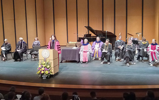 woman at podium speaking, several others seated behind her