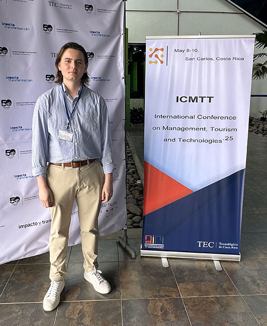 Landon DeKay, Alfred University MBA student, stands beside a conference banner at the International Conference on Management, Tourism, and Technologies in San Carlos, Costa Rica.