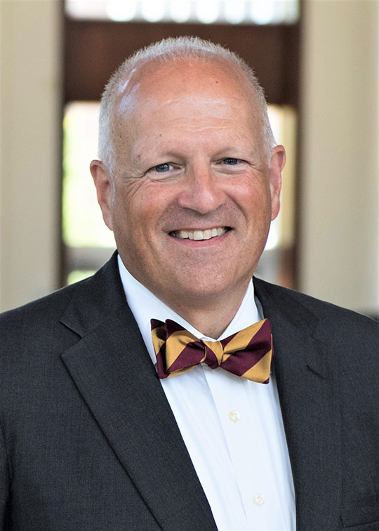 headshot of man with bow tie and suit coat, smiling