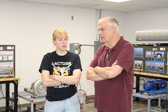 A student and professor have a discussion in an engineering lab at Alfred University, surrounded by electrical equipment and machinery.