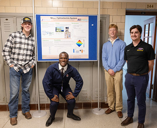 four people posed in front of a poster