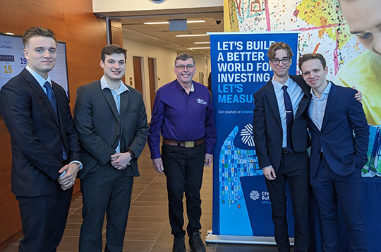 four young men in suits with professor in collared shirt, standing in a row smiling