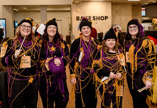five women wrapped in yarn, standing in a row