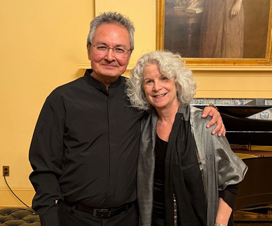 man and woman standing next to each other, piano in background